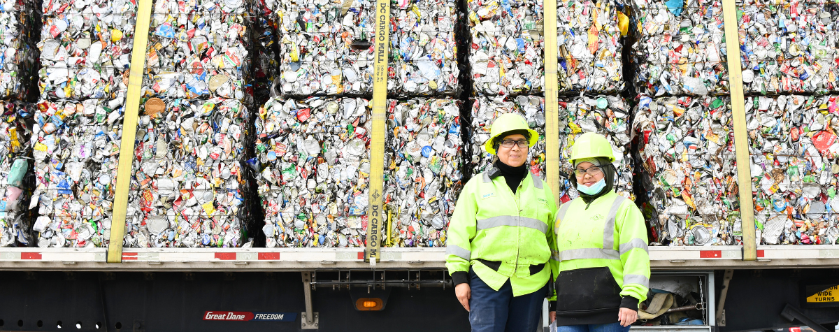 Two recycling staff pose next to bales of aluminum cans