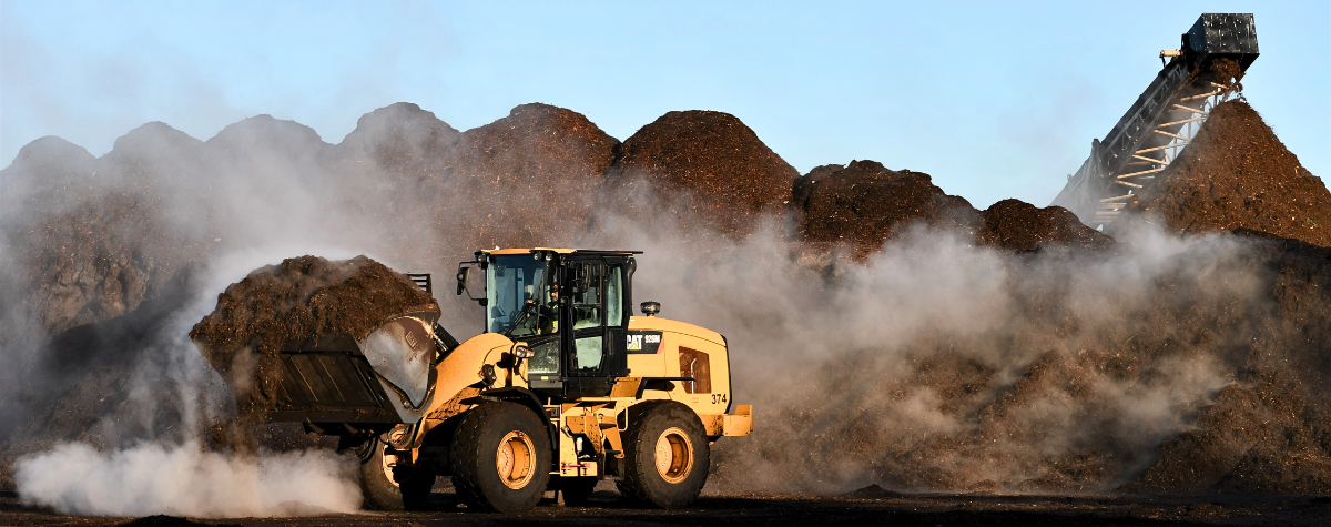 A loader drives by a steaming pile of compost